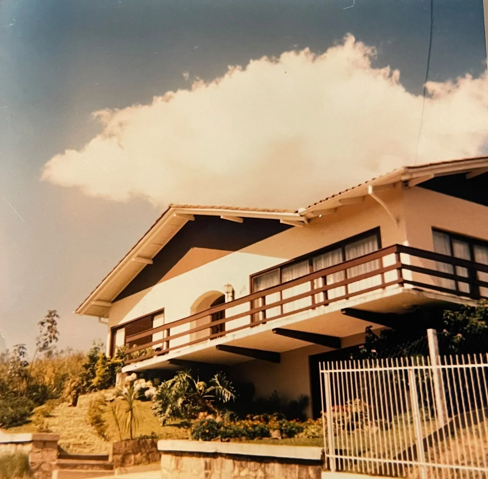 A casa pronta, de telhado de duas águas e sacada de madeira corrida, vista de baixo contra o céu azul