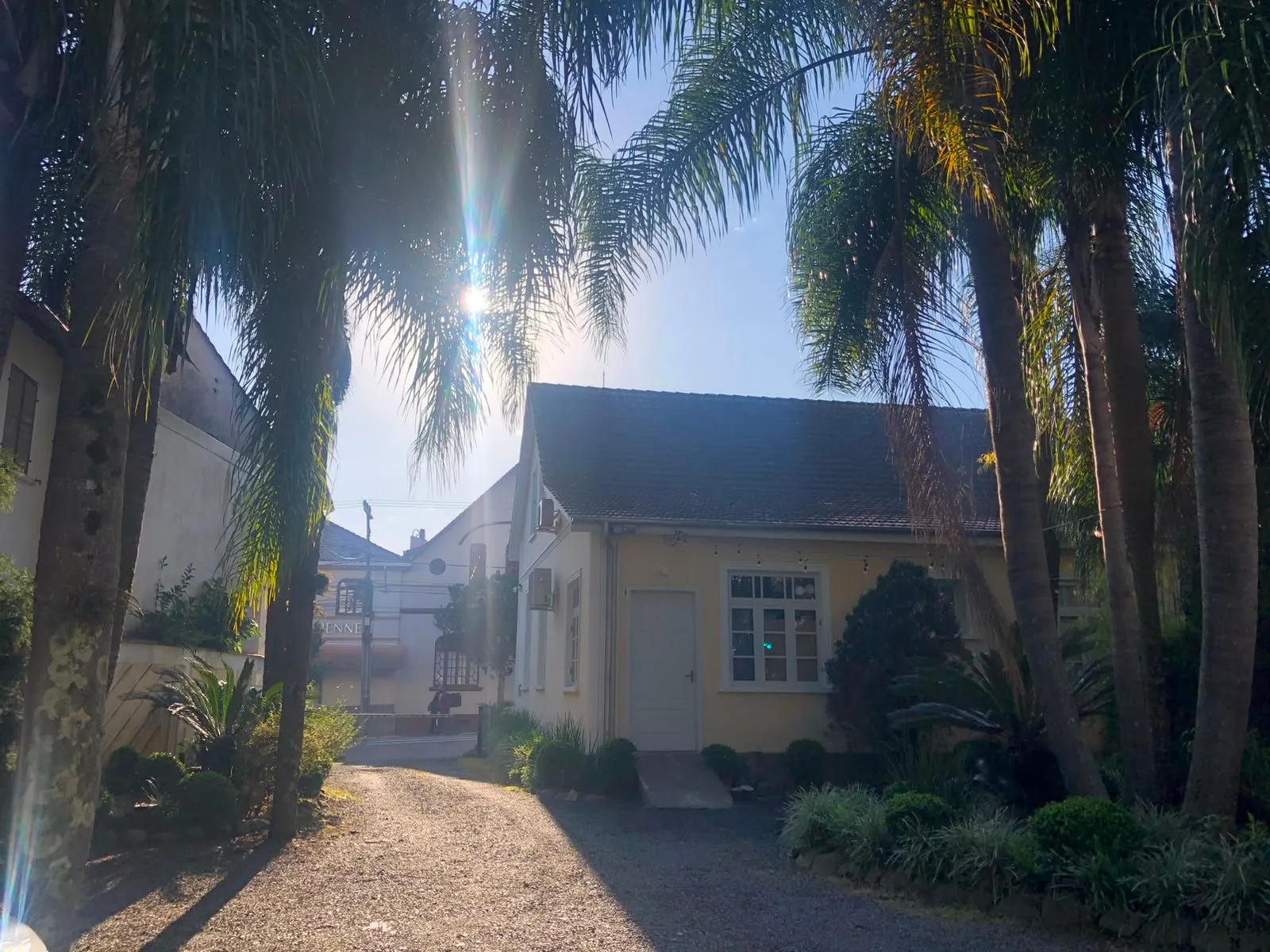 A mesma casa, hoje pintada de amarelo-claro e cercada de palmeiras e canteiros, com o sol atrás do telhado